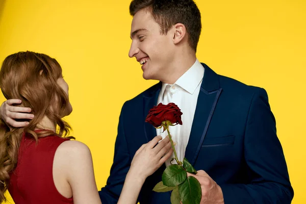 Amanti uomo e donna con una rosa rossa nelle loro mani abbracciando su uno sfondo giallo relazione sentimentale amore famiglia — Foto Stock