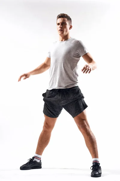 Спортивный человек в шортах и футболке делает упражнения на светлом фоне — стоковое фото
