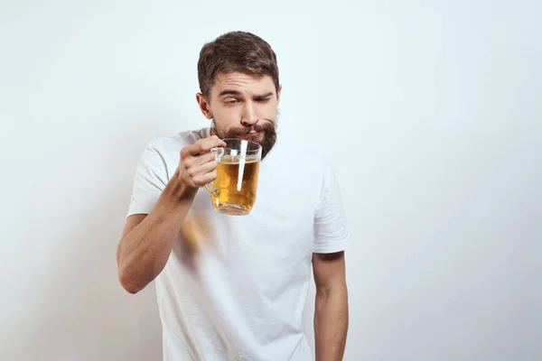 Hombre con una taza de cerveza en sus manos y una camiseta blanca fondo claro bigote barba emociones modelo — Foto de Stock