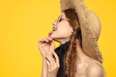 Şapkalı romantik bir kadın sarı arka planda eğleniyor ve güneş gözlüğü siyah kurdele modeli portresi takıyor.