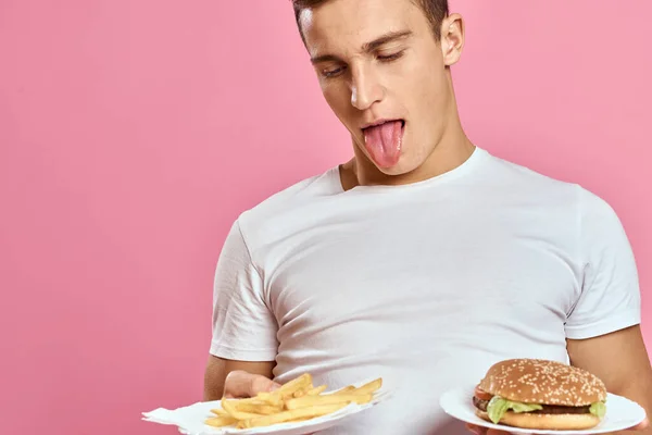 Guy hamburger fries and shows tongue on pink background — Stock Photo, Image