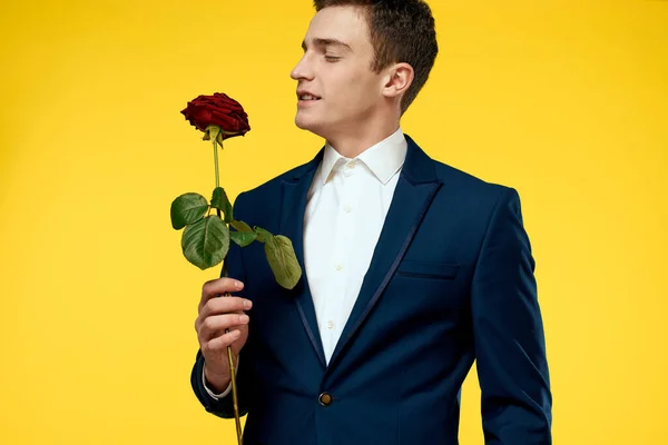 Jeune homme en costume classique avec une rose rouge à la main sur un fond jaune émotions recadré modèle de vue — Photo