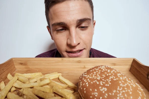 Önünde bir palet dolusu fast food patates kızartması ve yakın plan hamburger yiyen bir adam var. — Stok fotoğraf