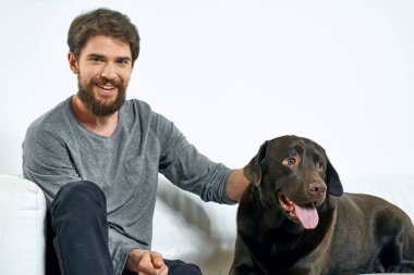 Beyaz bir kanepede siyah köpeği olan bir adam. Arka planda, yakın planda kesilen evcil hayvan insan arkadaş duyguları. Eğlenceli.