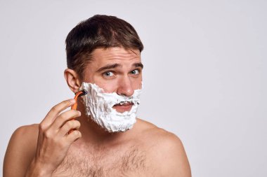 Yüzünde beyaz tıraş köpüğü olan yakışıklı bir adam ve jilet gibi omuzları olan temiz bir cilt.
