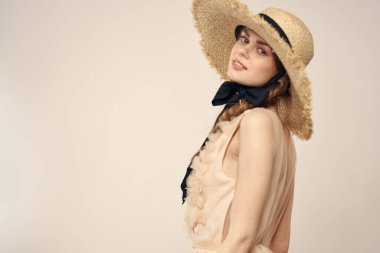 Hasır şapkalı, siyah kurdeleli ve arka planda açık bir elbise giyen hoş bir kız. Romantik bir model.