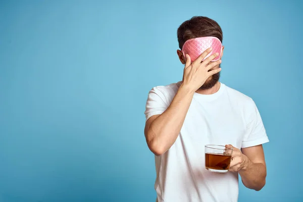 Homme avec masque de sommeil rose sur son visage et une tasse de thé dans ses mains vue recadrée gros plan fond bleu — Photo