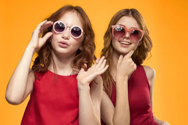 Happy sisters in red dresses on a yellow background are having fun and gesticulating Copy Space — Stock Photo, Image