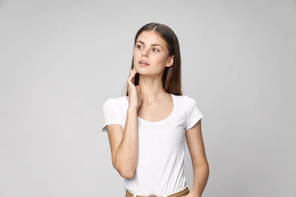 Una donna con una maglietta bianca tiene una mano vicino al viso, uno sguardo a lato — Foto Stock