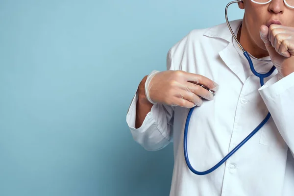 Медичний працівник у сукні та окулярах тримає стетоскоп у руках на блакитному тлі — стокове фото