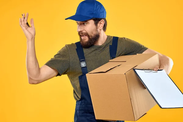 İşçi erkek kurye, kutu teslimatı, ambalaj belgeleri, sarı zemin — Stok fotoğraf