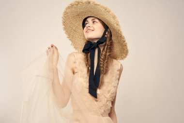 Hasır şapkalı, siyah kurdeleli ve arka planda açık bir elbise giyen hoş bir kız. Romantik bir model.