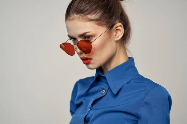 Mulher na moda em óculos de sol e uma camisa azul gesticulando com as mãos em um fundo leve vista cortada — Fotografia de Stock