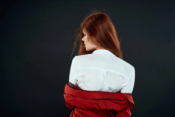 Woman in red jacket white shirt back view dark background