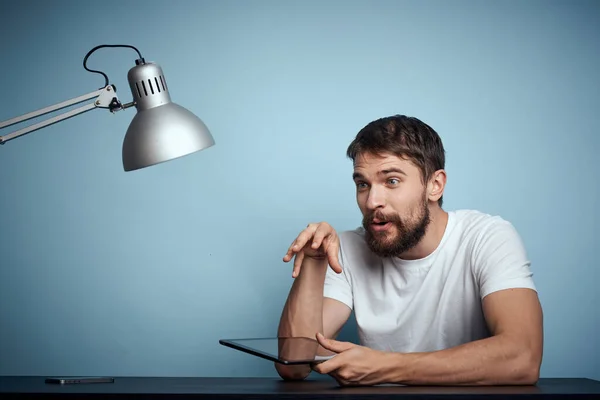 Homem com tablet à mesa dentro de casa e lâmpada escritório freelancer fundo azul — Fotografia de Stock