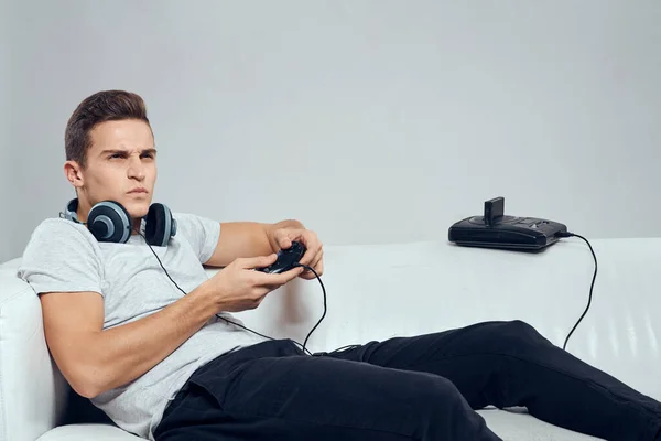 Un hombre yace en el sofá auriculares gamepad consolas tecnología entretenimiento videojuegos —  Fotos de Stock