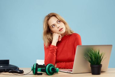 Dizüstü bilgisayar kulaklığının önündeki masada oturan bir kadın çevrimiçi yaşam tarzı mavi arka planda oynuyor.