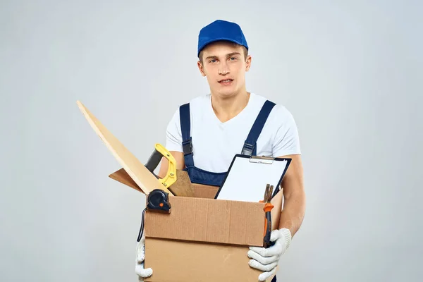 Man i arbetar uniform med en låda i händerna verktyg lastare leverans ljus bakgrund — Stockfoto