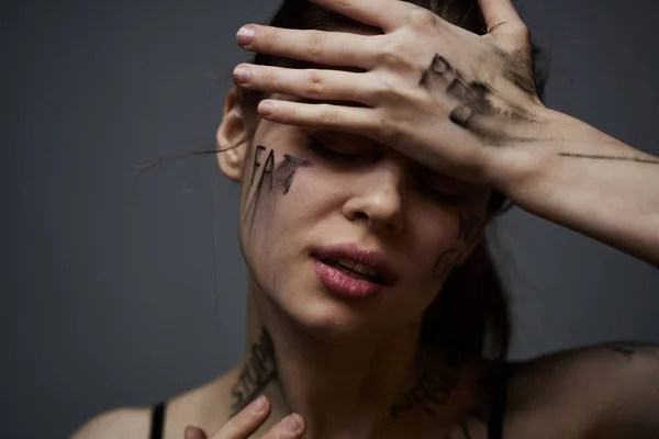 Ofendida mujer con inscripciones enojadas en su cuerpo se toca con las manos sobre un fondo gris agresión — Foto de Stock