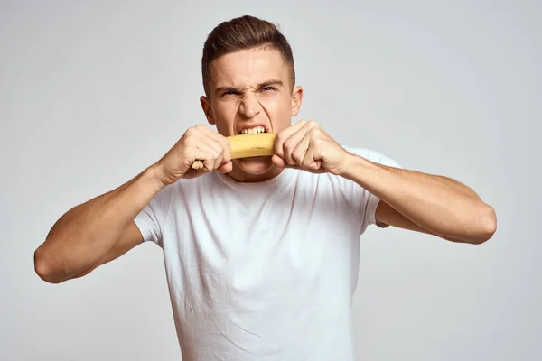 Ragazzo con una banana in mano su uno sfondo leggero divertimento emozioni luce sfondo bianco t-shirt modello — Foto Stock