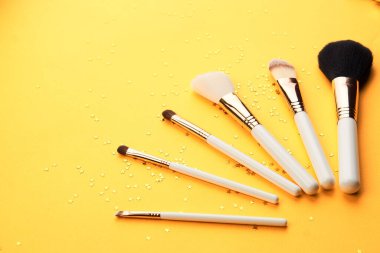 Sarı arka planda farklı boyutlarda makyaj fırçaları ve kırpılmış parıltılı görünüş