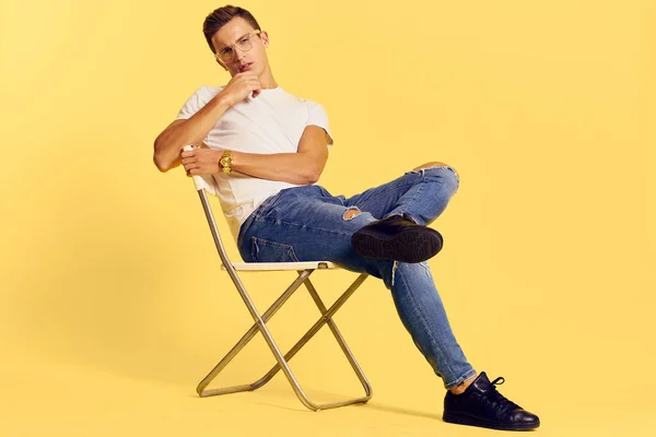 Χαριτωμένος άνθρωπος κάθεται σε μια καρέκλα λευκό t-shirt τζιν τρόπο ζωής μοντέρνο στυλ κίτρινο φόντο — Φωτογραφία Αρχείου