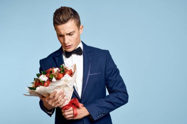 Bir buket çiçekli ve mavi arka planda papyonlu romantik bir adam.