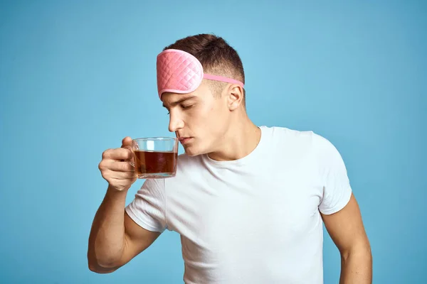 Hombre con máscara de sueño rosa y taza de té bebida alegre modelo desayuno — Foto de Stock