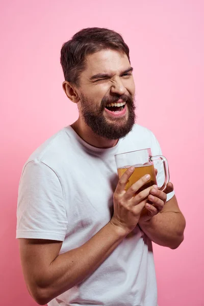 Bearded man med en mugg öl På en rosa bakgrund roliga känslor beskärda utsikt över en vit T-shirt berusad — Stockfoto