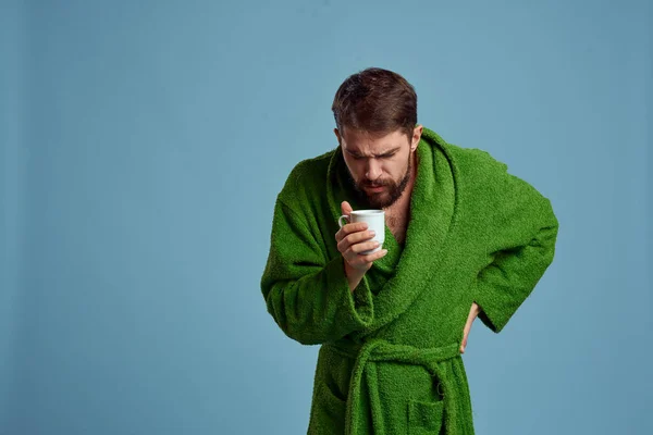 Frozen man in a warm robe with a cup of hot drink on a blue background cropped view — Stock Photo, Image