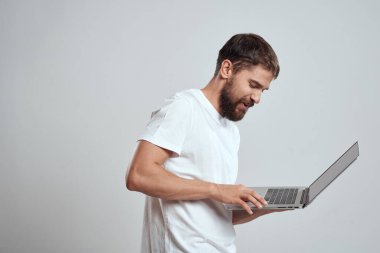 Elinde dizüstü bilgisayarla beyaz tişörtlü bir arka planı olan bir adamın duyguları yeni teknolojileri aydınlatır.