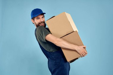 Elinde kutular olan işçi üniformalı adam teslimat servisinin mavi arka planında.