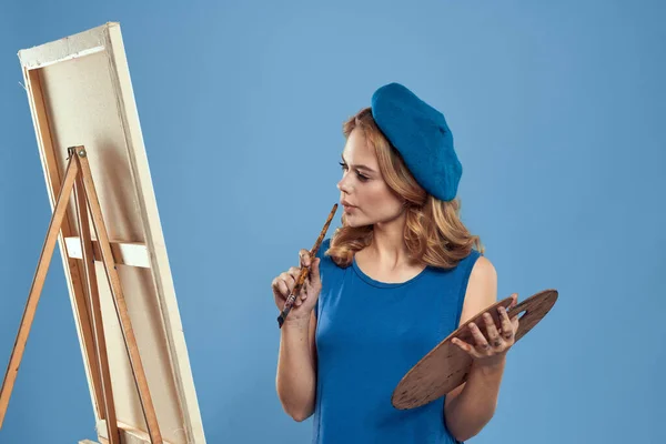 Frau Künstler blaue Baskenmütze Zeichnung Palette Staffelei Hobby Kreativität blauer Hintergrund — Stockfoto