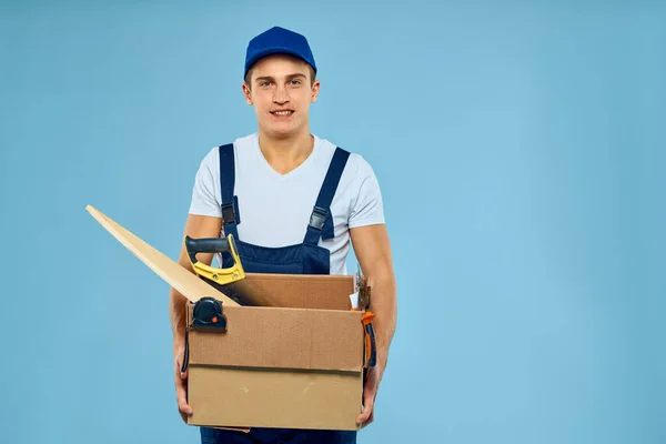 Trabalhador homem em caixa uniforme com ferramentas carregador entrega azul fundo — Fotografia de Stock