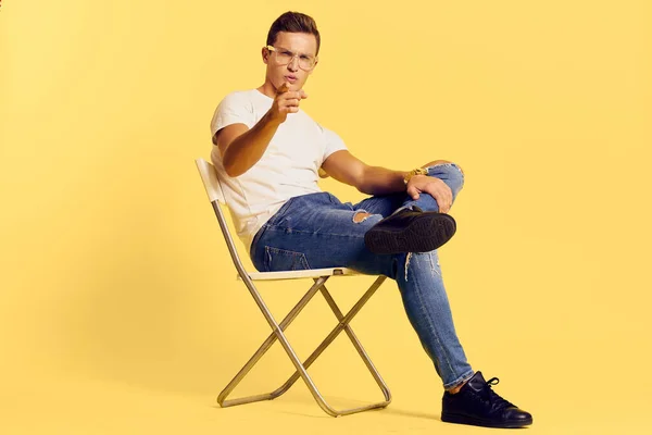 Cute man sitting on a chair white t-shirt jeans lifestyle modern style yellow background