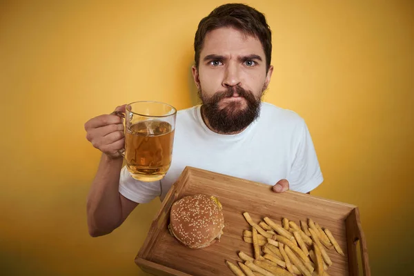 Homem barbudo com caneca de cerveja fast food dieta diversão álcool estilo de vida fundo amarelo — Fotografia de Stock
