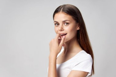 Beyaz tişörtlü bir kadın parmağını dudaklarına yaklaştırıyor ve ileriye bakıyor.