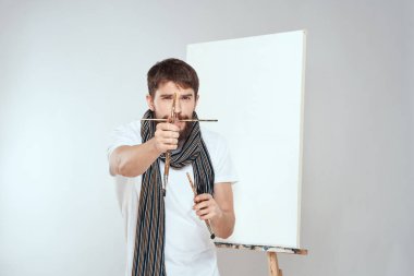 Erkek sanatçı, resim sehpasında elleriyle fırçalarken hobi olarak ensesinde hafif bir eşarp taşıyor.