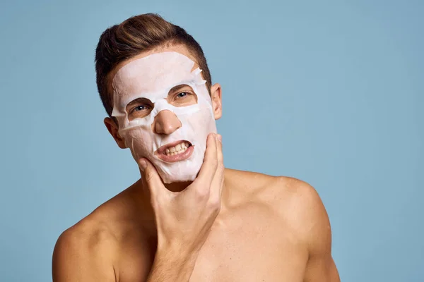 Uomo nudo con maschera nutriente bianca sul viso su sfondo blu vista ritagliata — Foto Stock