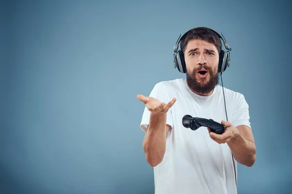 Mann mit Kopfhörer Controller in den Händen Spielkonsole Lifestyle Emotionen blauer Hintergrund weißes T-Shirt — Stockfoto