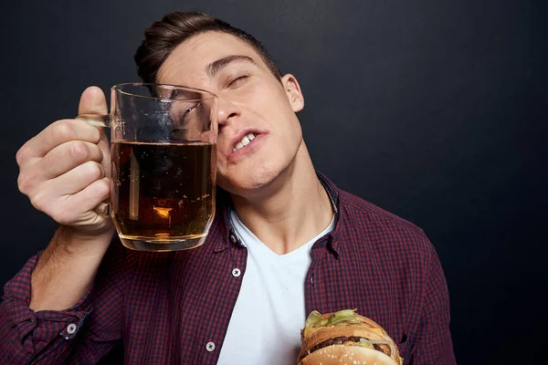Hombre con cerveza taza y hamburguesa en manos divertido estilo de vida estudio oscuro aislado fondo — Foto de Stock