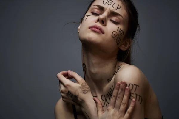 offended woman with angry inscriptions on her body touches herself with her hands on a gray background aggression