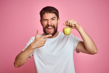 Pembe arka planda elmalı tatlı bir adam. Elleri kesilmiş beyaz tişörtlü, Uzay Kopyası.
