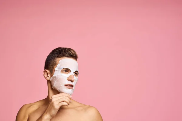 man with cleansing mask against black dots on his face on pink background cropped view and hands near face