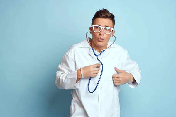 A medical worker in a dressing gown and glasses holds a stethoscope in his hands on a blue background cropped view — Stock Photo, Image