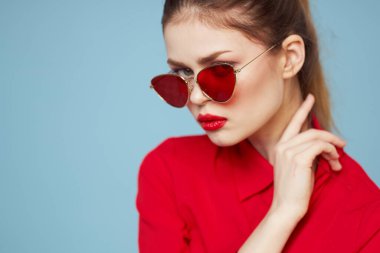 Koyu gözlükleri olan güzel bir kadın parlak makyajlı kırmızı dudaklar mavi arkaplanı büyülüyor.