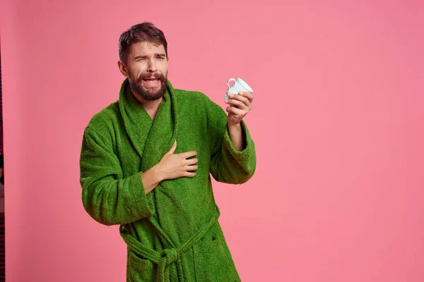 Mężczyzna z filiżanką herbaty na różowym tle przycięty widok emocji model zielony szlafrok — Zdjęcie stockowe