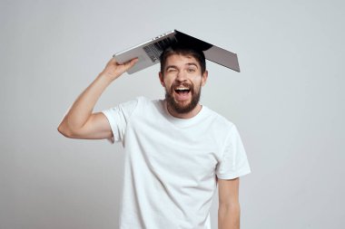 Elinde dizüstü bilgisayarla beyaz tişörtlü bir arka planı olan bir adamın duyguları yeni teknolojileri aydınlatır.