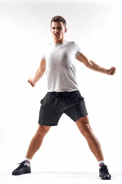 Un hombre deportivo en pantalones cortos y una camiseta larga hace ejercicios sobre un fondo claro — Foto de Stock