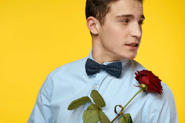 Elegant man in a suit with a red rose in his hands on a yellow background, cropped view — Stock Photo, Image